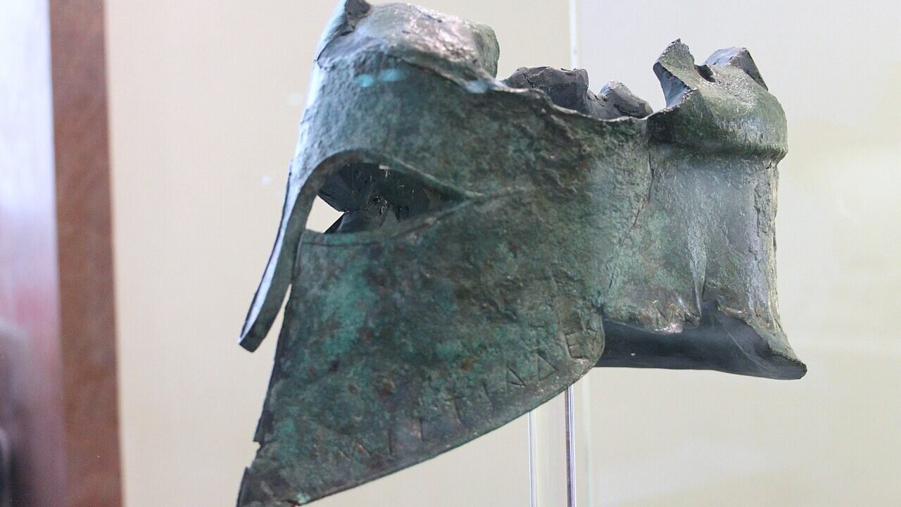 Coif grecesc de bronz de tip corintic, expus într-o vitrină de muzeu