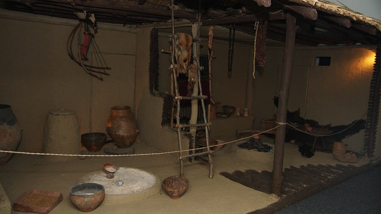 Reconstituire a interiorului unei case cucuteniene, cu vatră, vase și râșniță