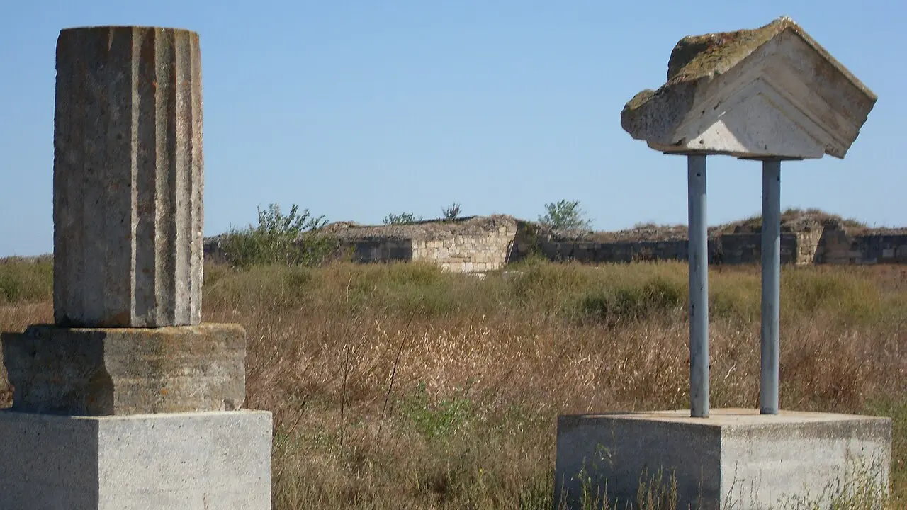 Coloană și fronton de piatră în situl arheologic Histria, cu zidul incintei târzii în fundal