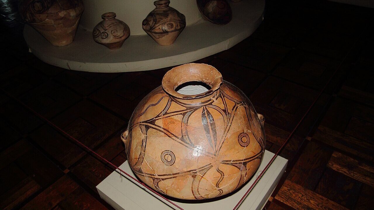 Vas ceramic Cucuteni cu decor spiralat pictat, expus într-o vitrină de muzeu alături de alte piese