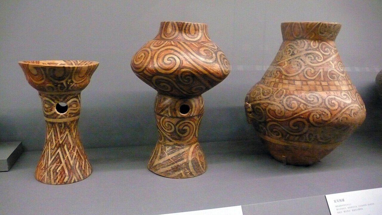 Trei vase pictate Cucuteni, un castron pe picior, un vas pe picior și o amforă, într-o vitrină de muzeu