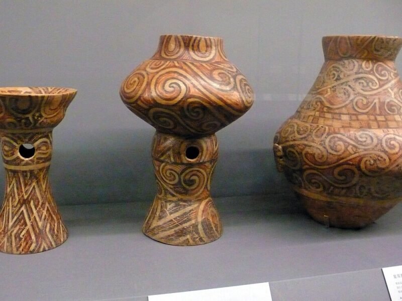 Trei vase pictate Cucuteni, un castron pe picior, un vas pe picior și o amforă, într-o vitrină de muzeu