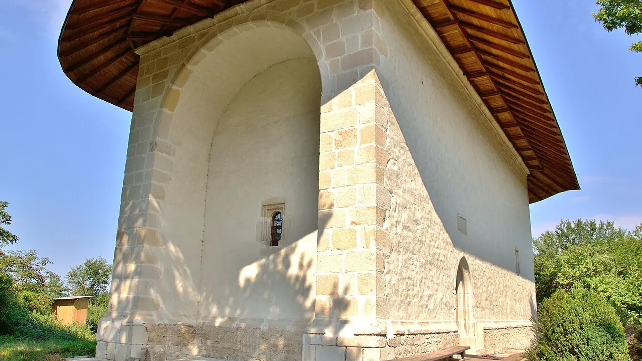 Biserica de piatră din Reuseni, cu acoperiș înalt și turlă, văzută din curte