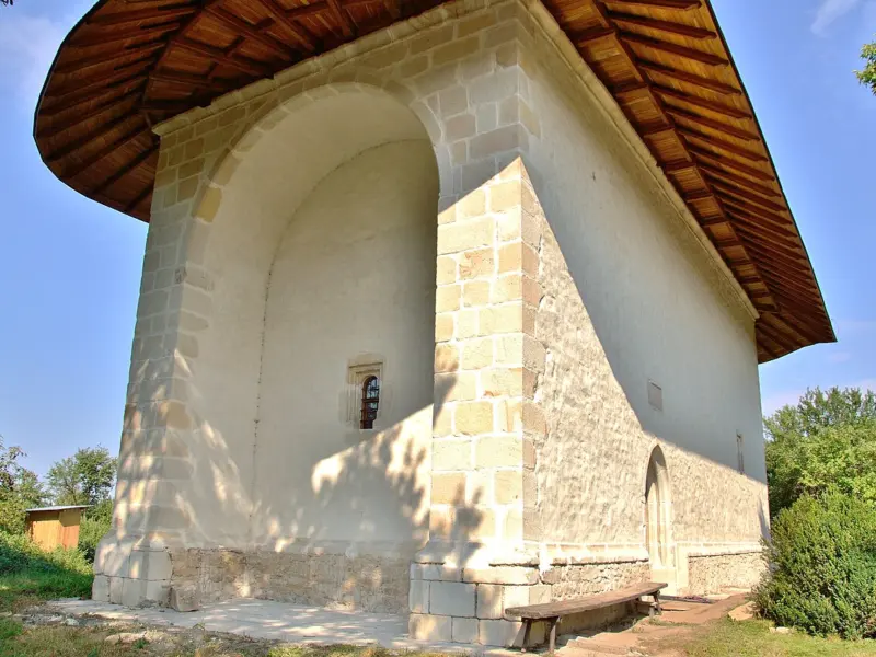 Biserica de piatră din Reuseni, cu acoperiș înalt și turlă, văzută din curte