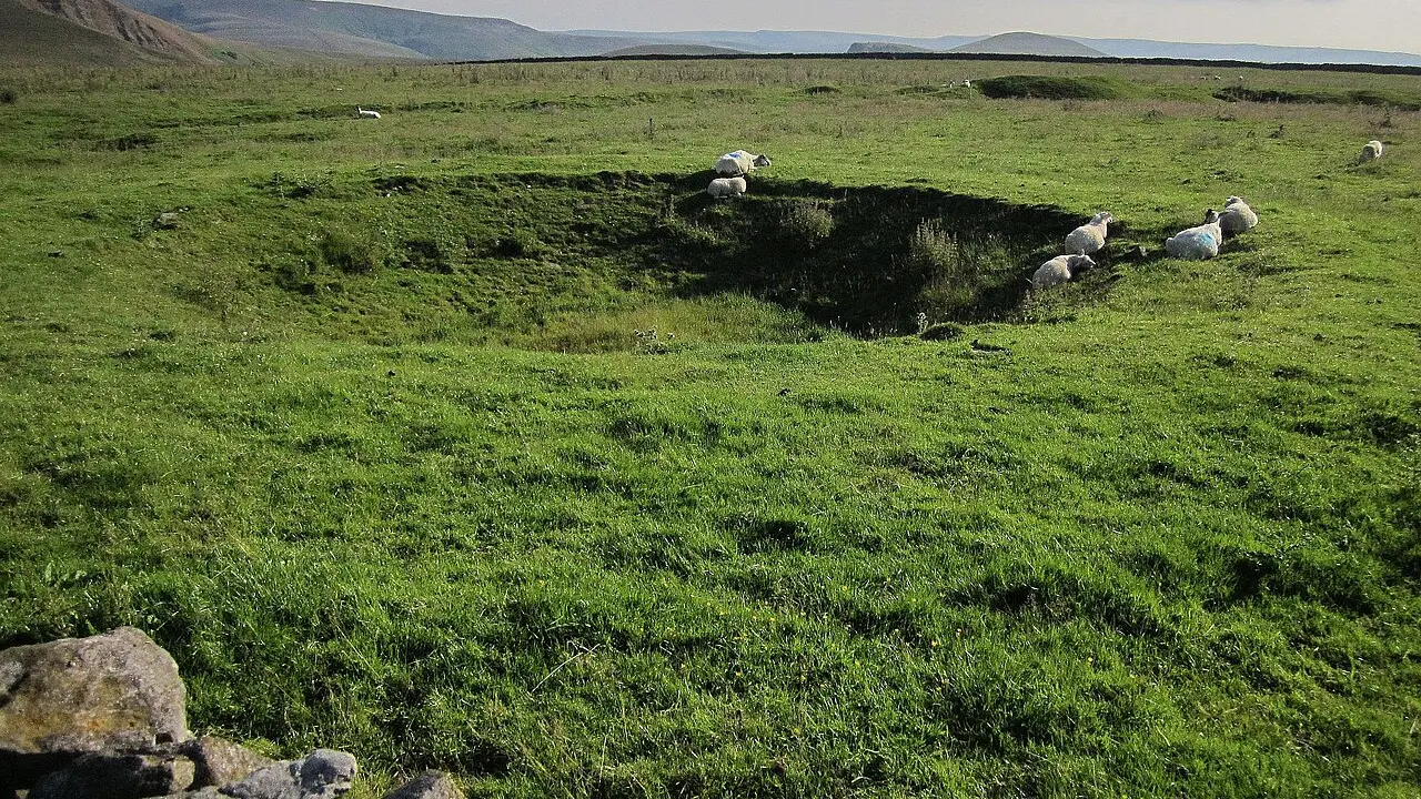 Gura unei mine vechi de plumb, împrejmuită, într-un câmp din Peak District
