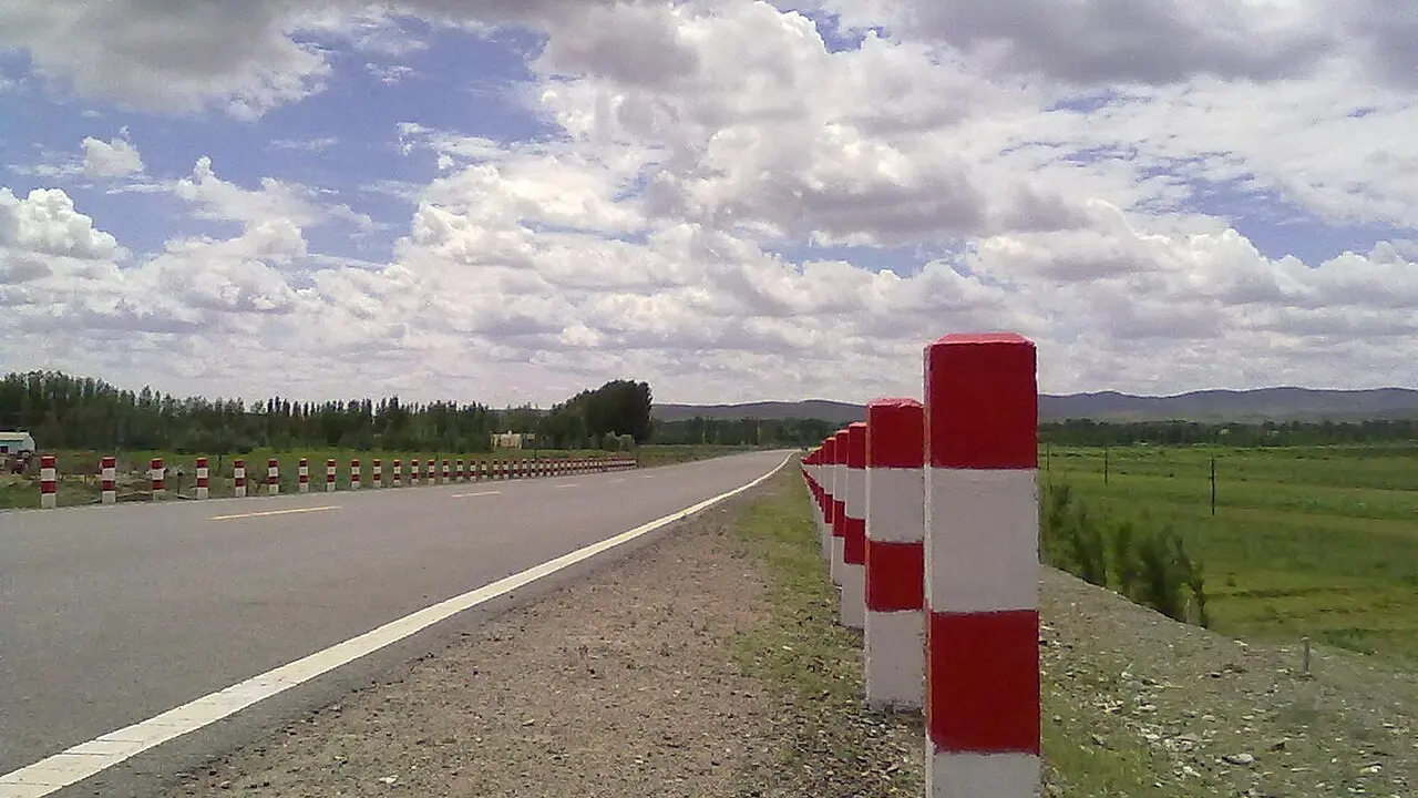 Drum asfaltat printr-o câmpie verde, cu dealuri la orizont, în ținutul Fuyun din Xinjiang